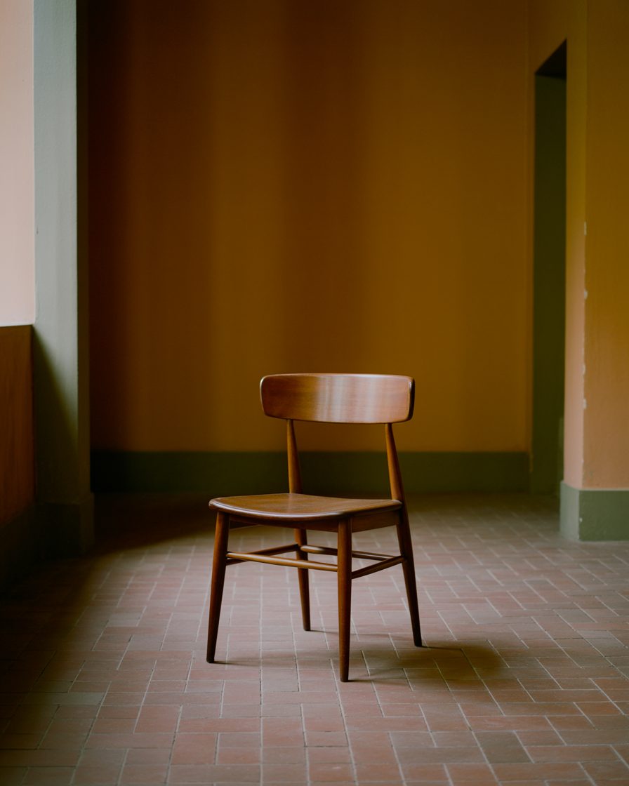 A single empty wooden chair in a warm, bare room